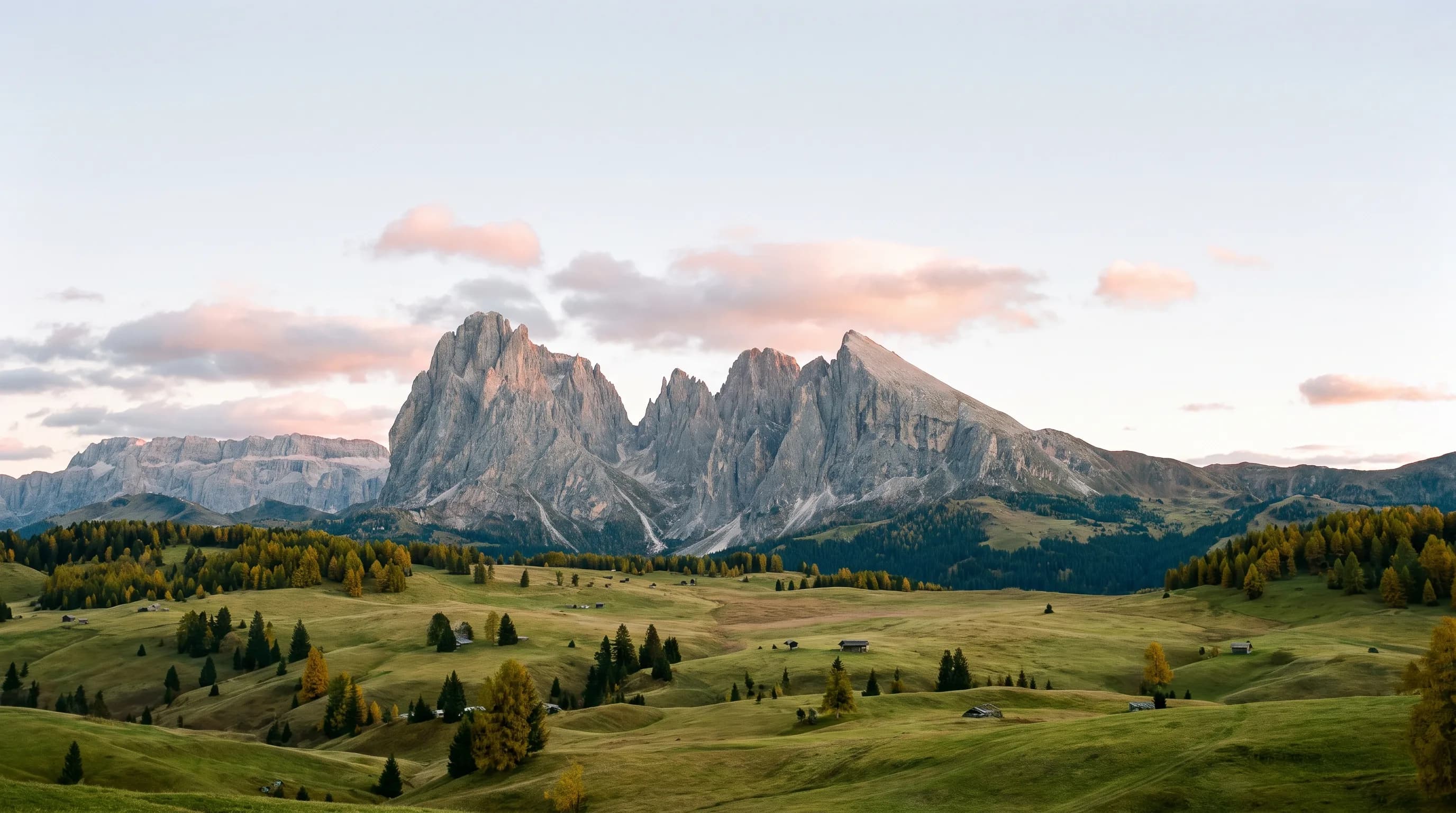 Sharp Dolomite mountain peaks above a quiet alpine valley in soft seasonal light.